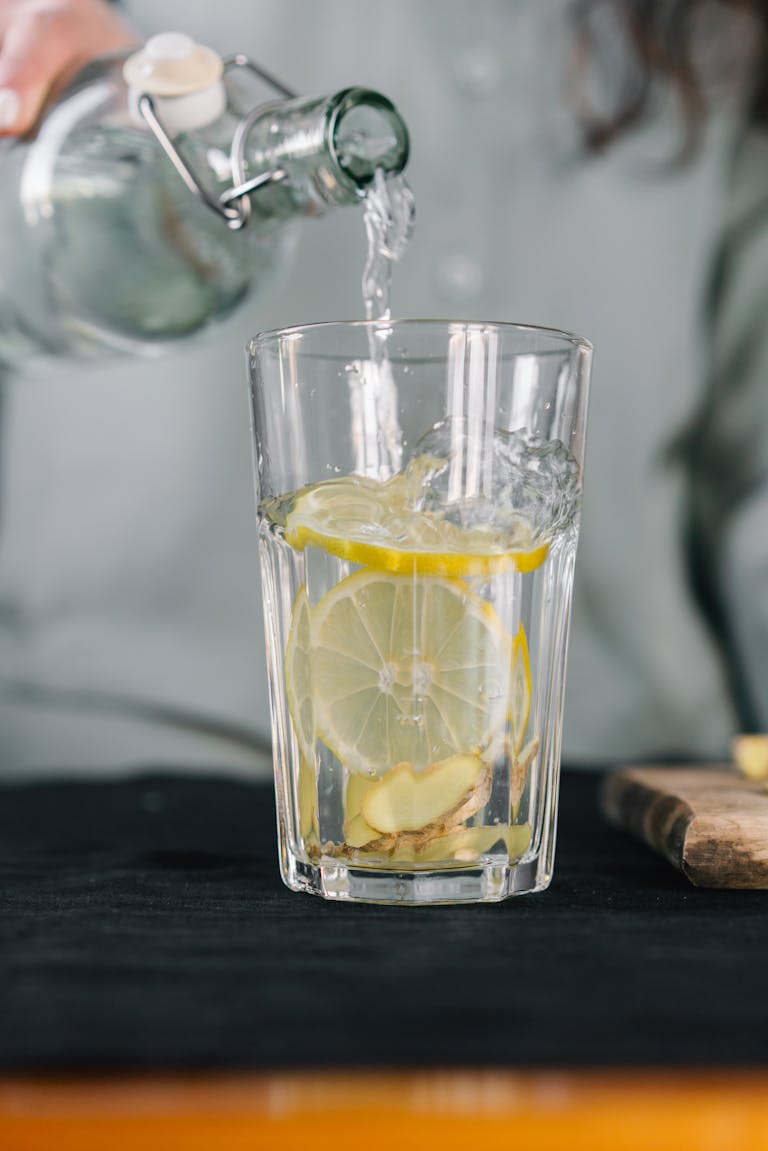 A glass of lemon water with ginger being poured for a refreshing detox drink.